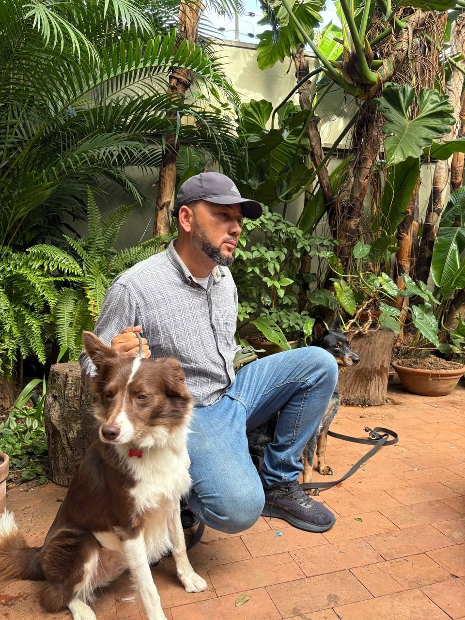 Retrato do Flávio agachado com um cão border collie em um jardim, olhando para o animal com atenção
